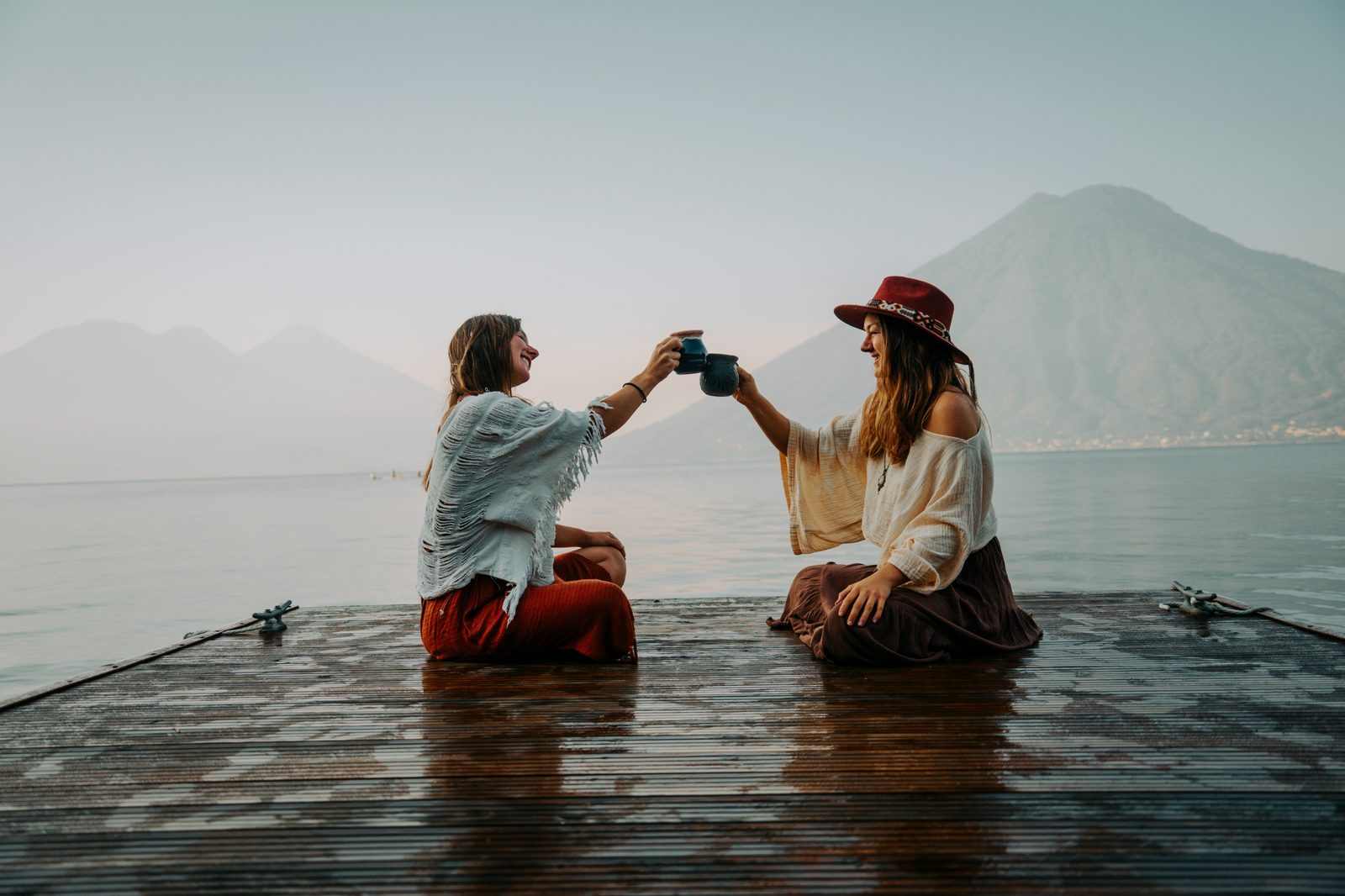 Two women sharing ceremonial cacao on a dock overlooking Lake Atitlán and its volcanoes
